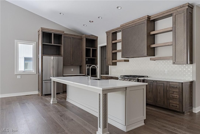 kitchen with stainless steel appliances, vaulted ceiling, sink, dark hardwood / wood-style floors, and an island with sink