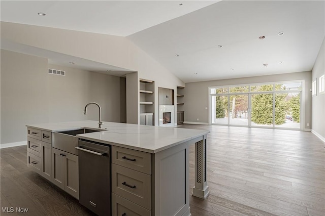 kitchen featuring light stone counters, gray cabinetry, vaulted ceiling, a kitchen island with sink, and dishwasher