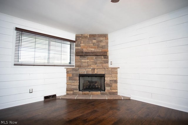 unfurnished living room with a stone fireplace, wooden walls, and hardwood / wood-style floors