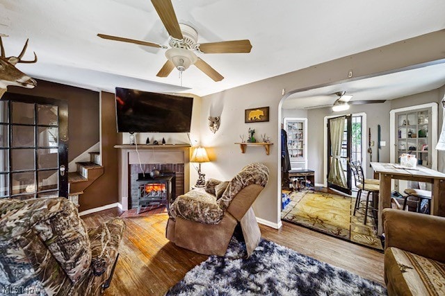 living room featuring wood-type flooring, a brick fireplace, and ceiling fan