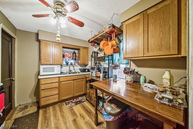 kitchen with ceiling fan, light hardwood / wood-style floors, a textured ceiling, and sink