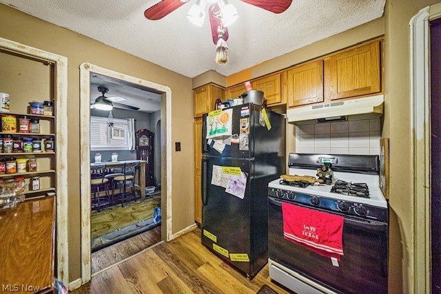 kitchen with white gas range, black fridge, ceiling fan, and hardwood / wood-style flooring