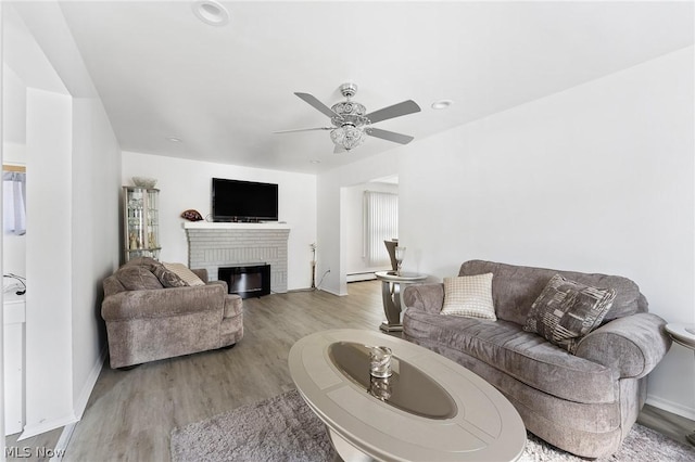 living room with a baseboard heating unit, a brick fireplace, light hardwood / wood-style flooring, and ceiling fan