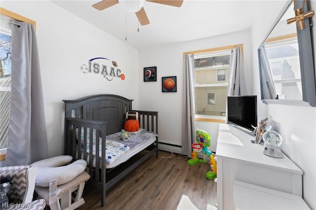 bedroom with ceiling fan, a baseboard heating unit, dark hardwood / wood-style floors, and a crib