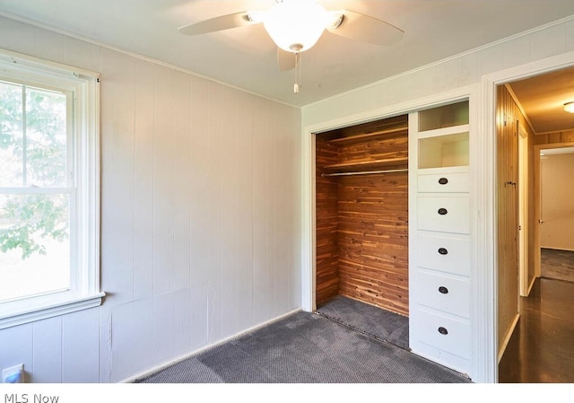 unfurnished bedroom with ceiling fan, a closet, wood walls, and dark colored carpet