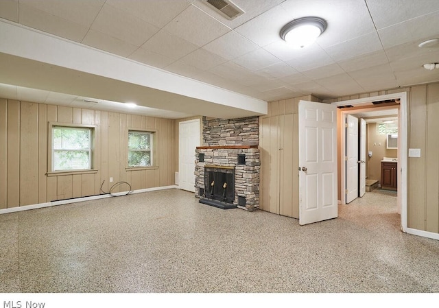 unfurnished living room featuring a stone fireplace, wooden walls, and a paneled ceiling