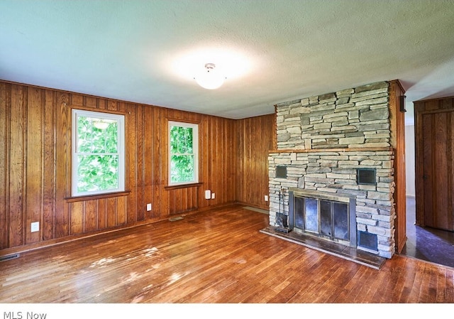 unfurnished living room with a textured ceiling, a fireplace, wood-type flooring, and wood walls