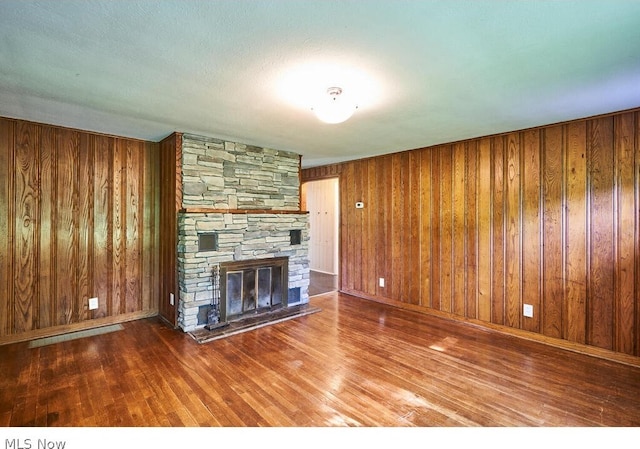 unfurnished living room featuring a stone fireplace, wood walls, and hardwood / wood-style flooring