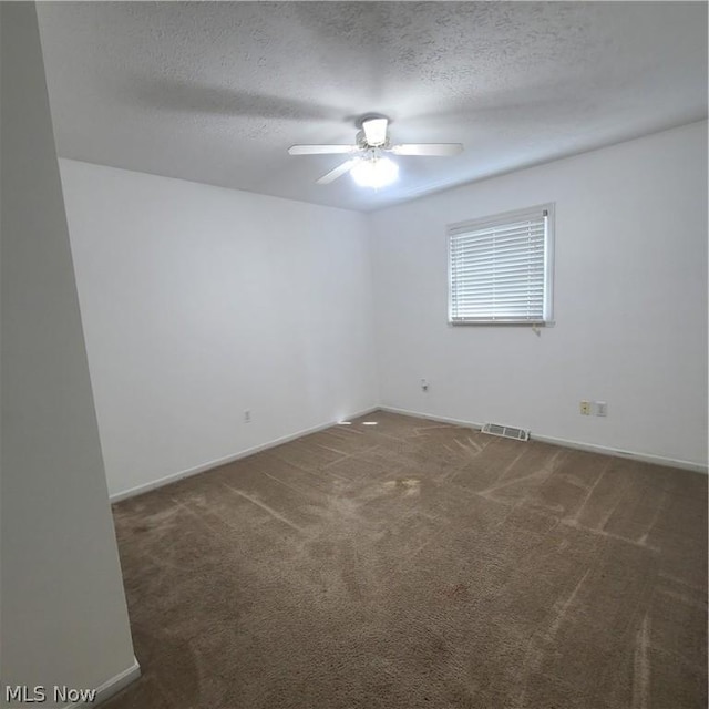 carpeted spare room with a textured ceiling, visible vents, a ceiling fan, and baseboards