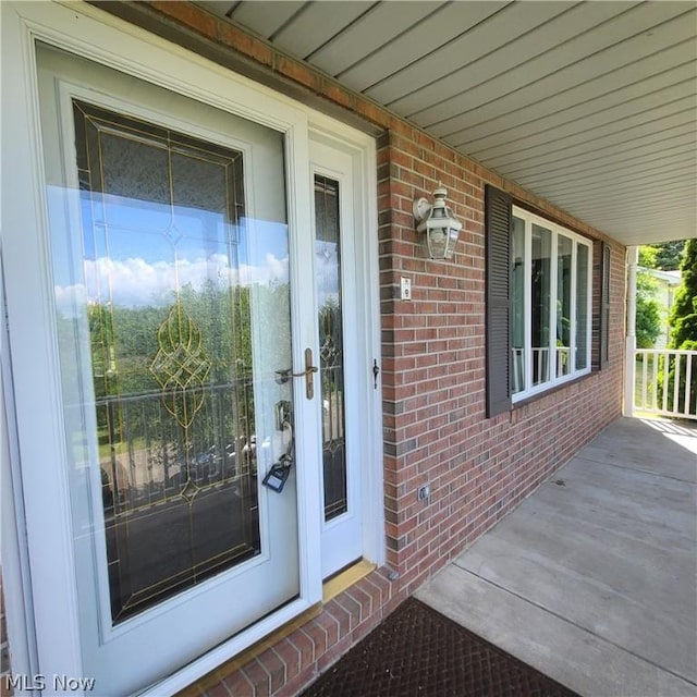 doorway to property with a porch and brick siding