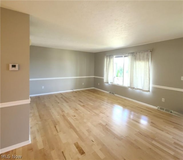 empty room with visible vents, light wood-style flooring, and baseboards