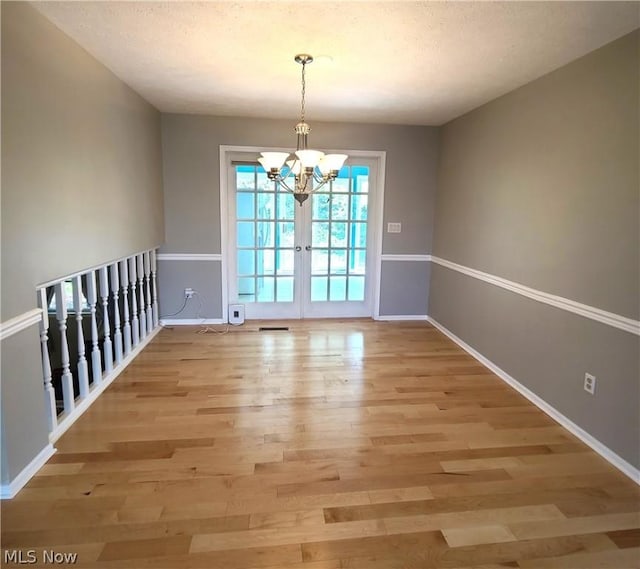 unfurnished dining area with baseboards, a notable chandelier, a textured ceiling, and light wood finished floors