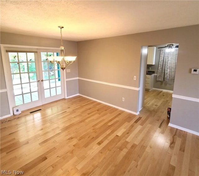 unfurnished dining area featuring baseboards, visible vents, an inviting chandelier, a textured ceiling, and light wood-type flooring