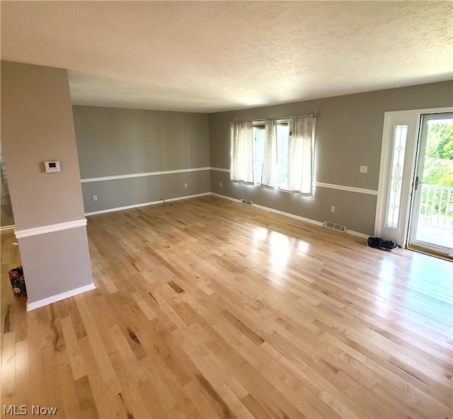 unfurnished living room featuring baseboards, visible vents, light wood-style flooring, and a textured ceiling