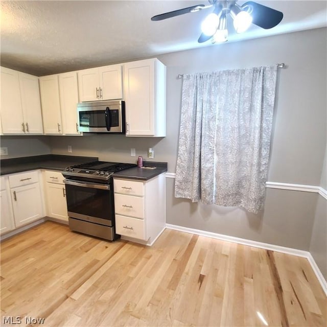 kitchen featuring light wood-style flooring, stainless steel appliances, white cabinetry, baseboards, and dark countertops