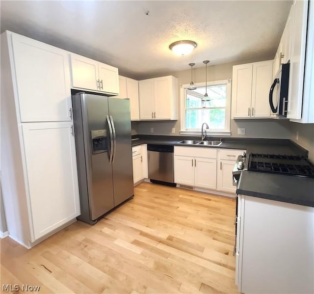 kitchen featuring white cabinets, dark countertops, light wood-style flooring, stainless steel appliances, and a sink