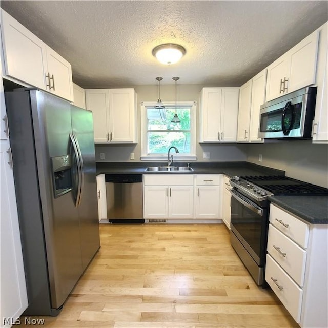 kitchen featuring stainless steel appliances, dark countertops, white cabinetry, a sink, and light wood-type flooring