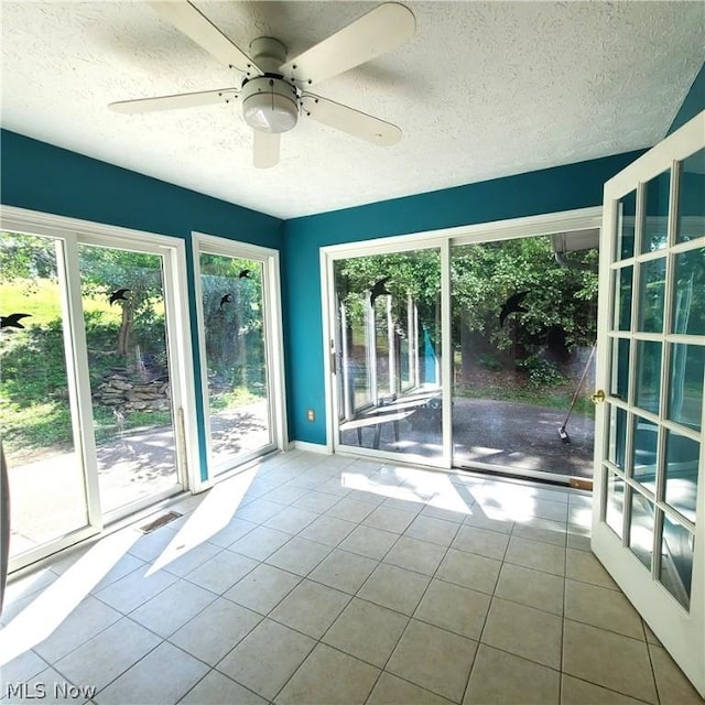 tiled empty room with a textured ceiling, visible vents, a wealth of natural light, and a ceiling fan