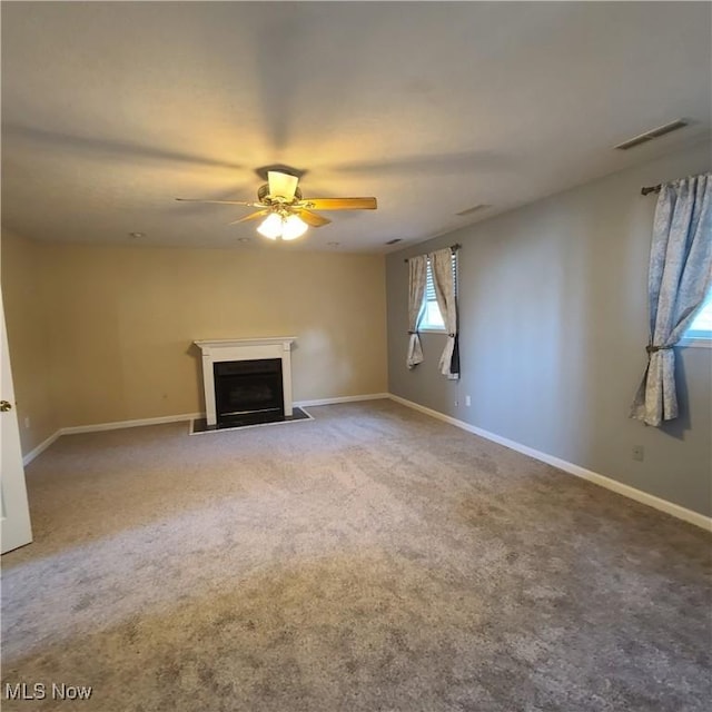 unfurnished living room with carpet floors, a fireplace with flush hearth, visible vents, and baseboards