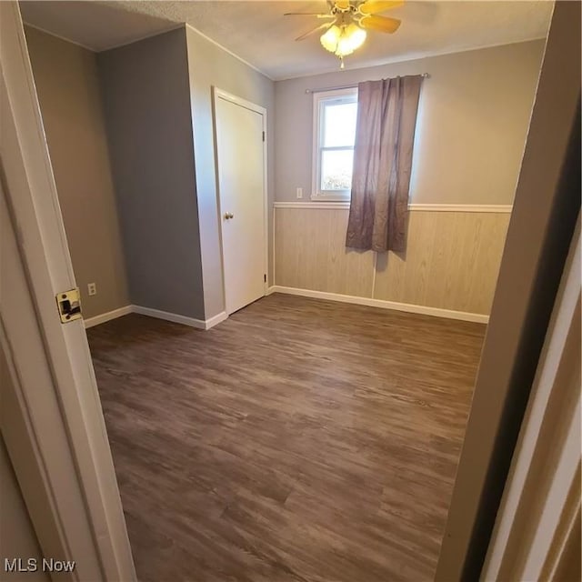 unfurnished bedroom with dark wood-style floors, a wainscoted wall, and a ceiling fan