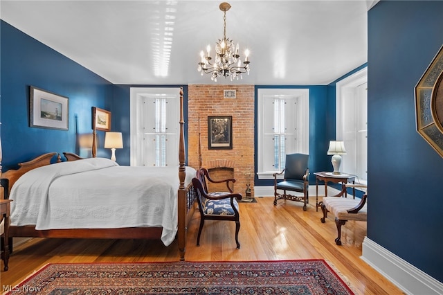 bedroom with hardwood / wood-style floors, a chandelier, and a brick fireplace