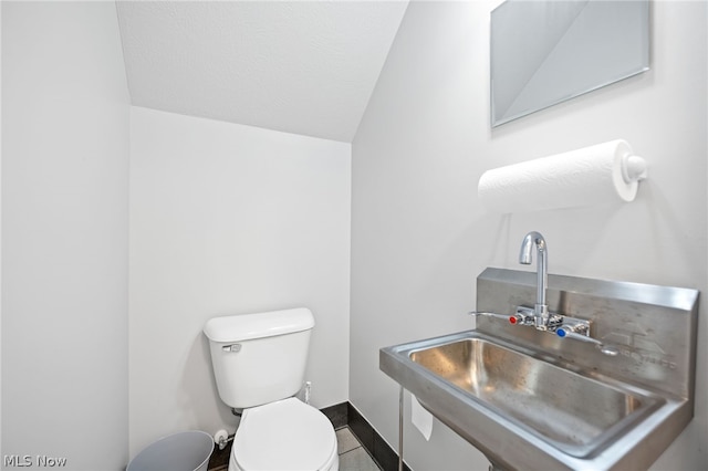 bathroom with toilet, tile patterned flooring, vaulted ceiling, and sink