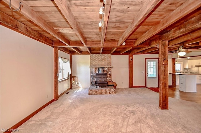 unfurnished living room with a wood stove, light carpet, ceiling fan, and wooden ceiling