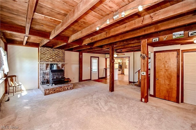 unfurnished living room with a wood stove, light carpet, rail lighting, ceiling fan, and beam ceiling