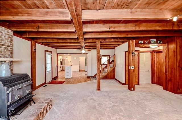 basement featuring a wood stove, light carpet, ceiling fan, and wood ceiling