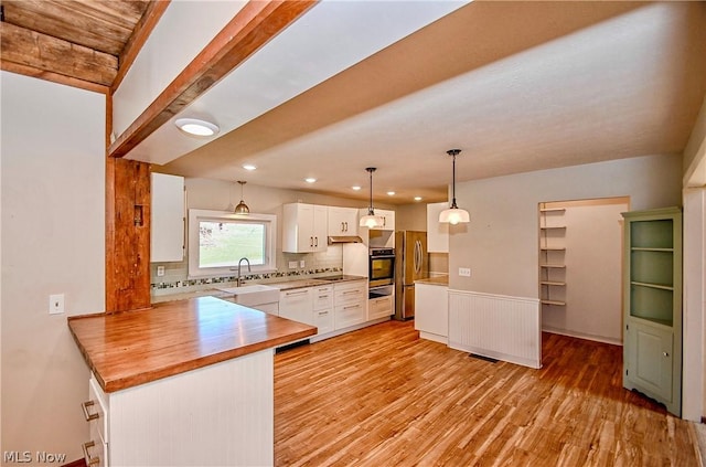 kitchen featuring pendant lighting, white cabinets, tasteful backsplash, wall oven, and stainless steel refrigerator