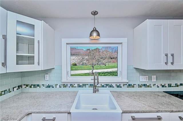 kitchen with backsplash, white cabinetry, sink, and hanging light fixtures