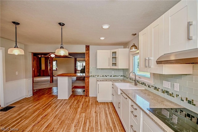 kitchen with light stone countertops, white cabinetry, sink, black electric stovetop, and light wood-type flooring