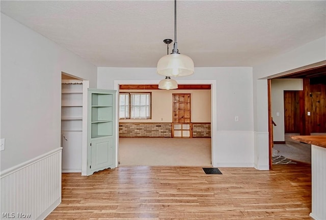 unfurnished dining area featuring a textured ceiling, light hardwood / wood-style floors, and built in features