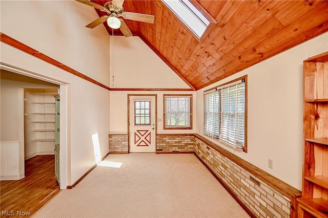 carpeted spare room featuring wood ceiling, ceiling fan, vaulted ceiling with skylight, and brick wall