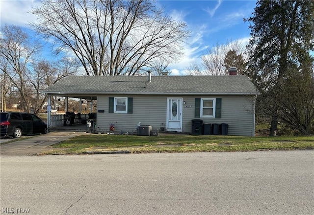 ranch-style home with driveway, a shingled roof, a carport, central AC unit, and a chimney