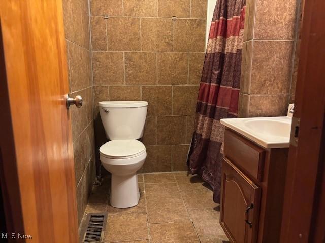 bathroom featuring vanity, tile walls, and toilet