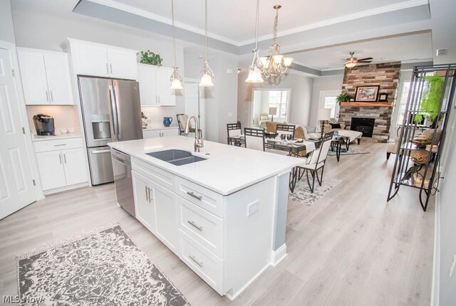 kitchen featuring light hardwood / wood-style flooring, ceiling fan with notable chandelier, a center island with sink, a stone fireplace, and sink