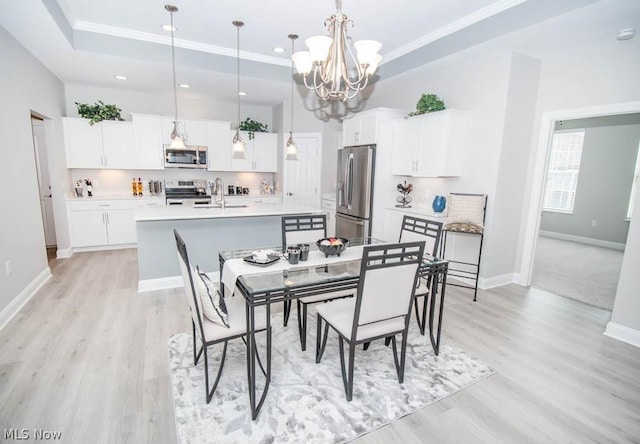 dining area with a tray ceiling, sink, a notable chandelier, and light hardwood / wood-style flooring