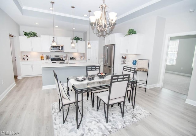 dining room with a raised ceiling, ornamental molding, sink, and light wood-type flooring