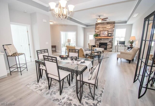 dining room featuring light hardwood / wood-style floors, a fireplace, ceiling fan with notable chandelier, and a raised ceiling