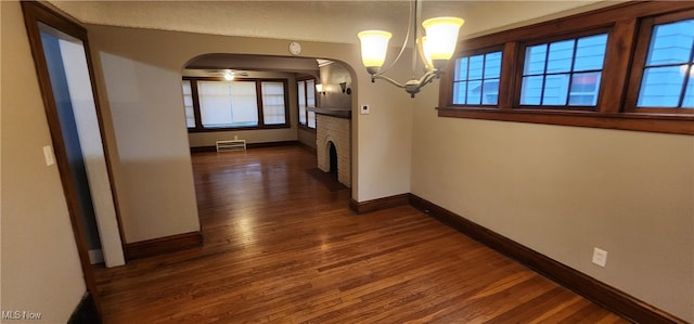 unfurnished dining area featuring a brick fireplace, dark wood-type flooring, and an inviting chandelier