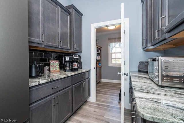 kitchen with light stone countertops, backsplash, light hardwood / wood-style floors, and dark brown cabinetry