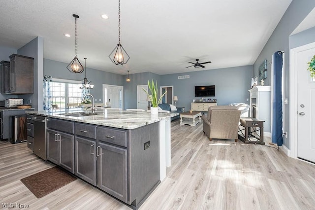 kitchen featuring ceiling fan, sink, hanging light fixtures, light stone counters, and a center island with sink