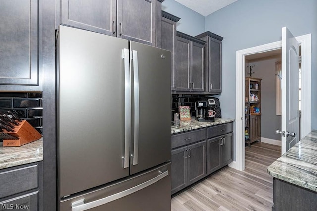 kitchen featuring light stone counters, light wood-type flooring, stainless steel refrigerator, and tasteful backsplash