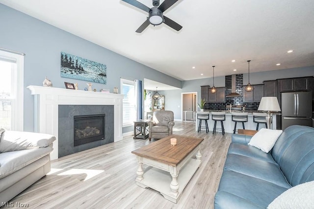 living room with a tile fireplace, ceiling fan, and light wood-type flooring