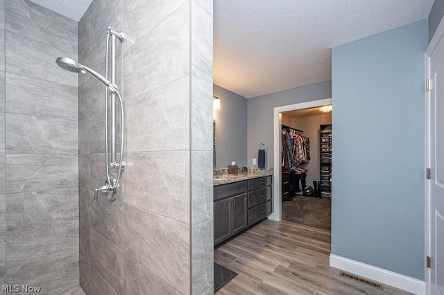 bathroom with vanity, hardwood / wood-style floors, a textured ceiling, and tiled shower