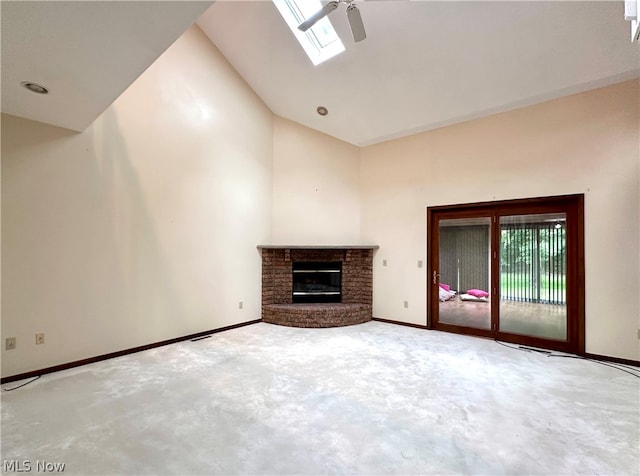 unfurnished living room featuring a brick fireplace, carpet flooring, lofted ceiling with skylight, and ceiling fan