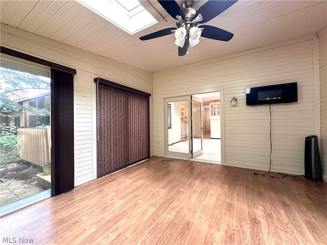 unfurnished bedroom featuring wood walls, wood-type flooring, a skylight, and access to exterior