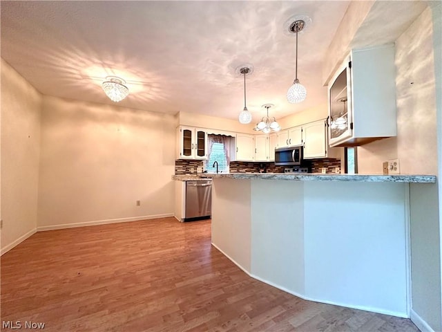 kitchen featuring decorative backsplash, a peninsula, wood finished floors, white cabinets, and stainless steel appliances