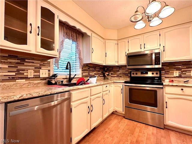 kitchen featuring light wood finished floors, tasteful backsplash, glass insert cabinets, appliances with stainless steel finishes, and a sink